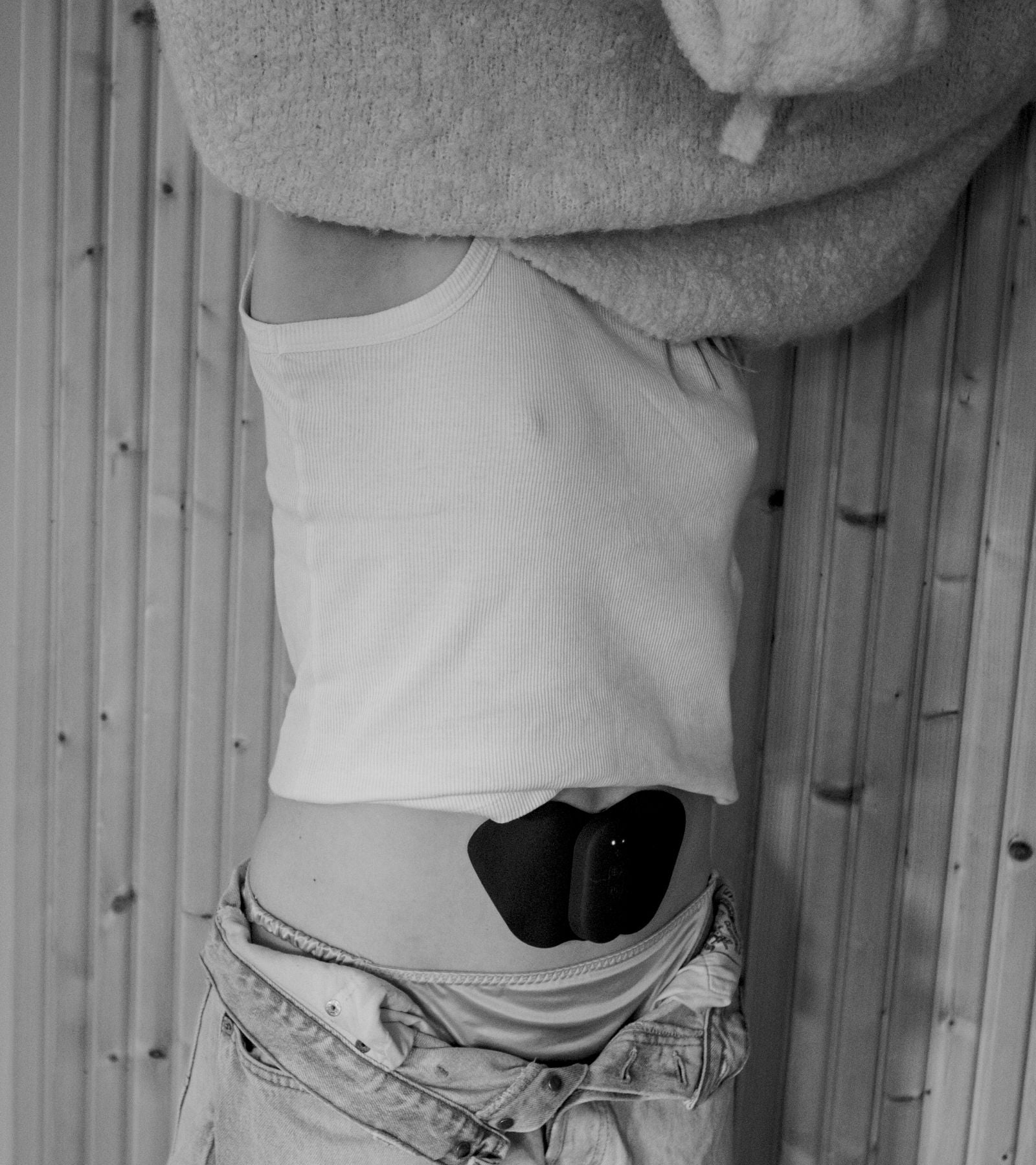 Kvinna bär en TENS-apparat på magen och känner lindring av menssmärtor.