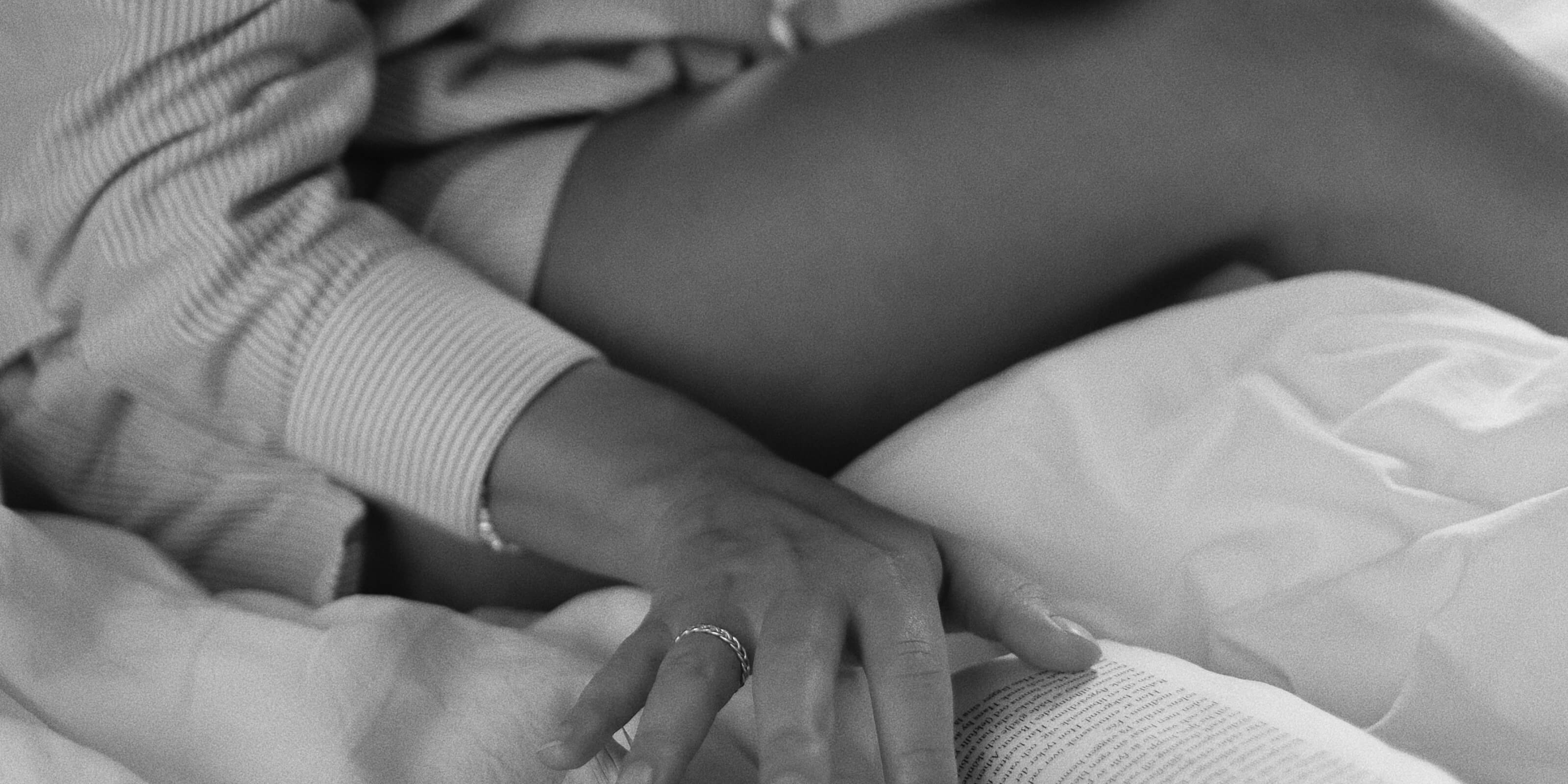 En närbild av kvinna i randig skjorta sitter på en säng och rör försiktigt vid en uppslagen bok. Scenen förmedlar en mysig, avslappnad morgonkänsla.